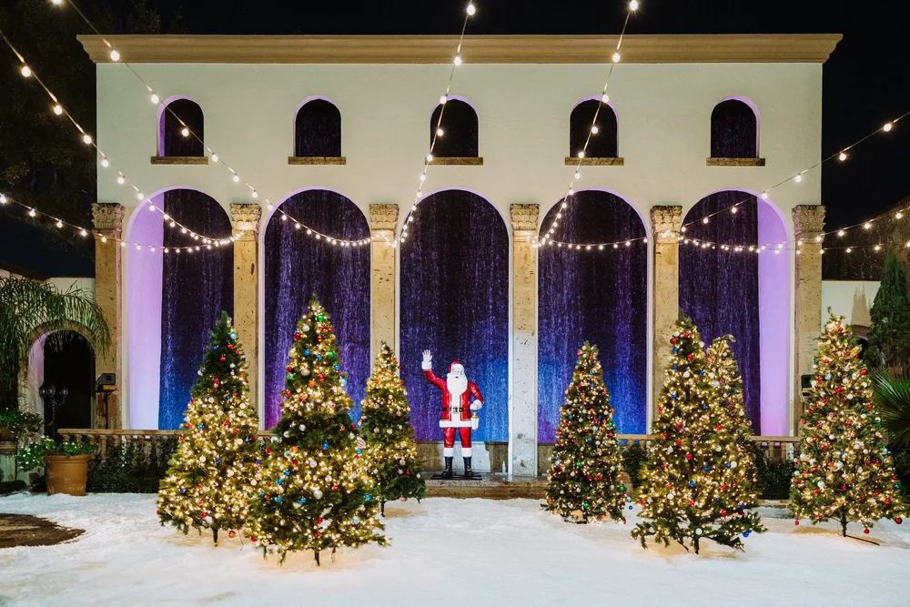 Santa greeting guests beside decorated Christmas trees at a holiday party at The Bell Tower on 34th in Houston